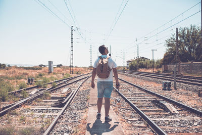 Rear view of man standing on railroad tracks against sky