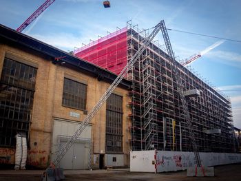 Low angle view of crane by building against sky