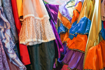 Festive costumes and dresses of various colors hanging on hangers in a store