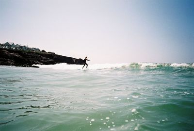 Surfer surfing on sea against clear sky