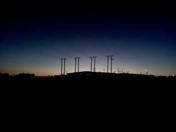 Silhouette electricity pylons against clear sky at sunset