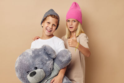 Portrait of sibling with stuffed toy against beige background