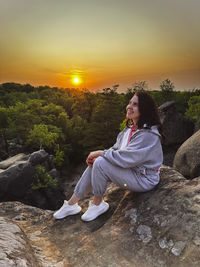 Portrait of young woman standing on rock against sky during sunset