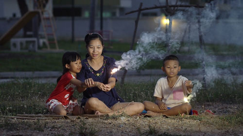 Family holding sparklers while sitting on field