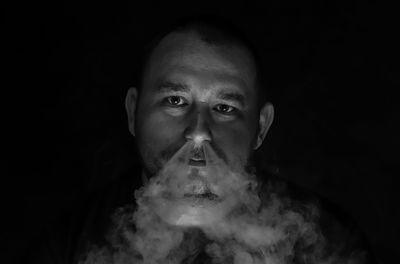 Portrait of man smoking cigarette against black background