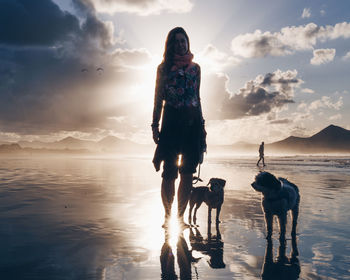 Rear view of woman walking at beach against sky during sunset