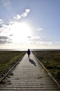 Rear view of woman walking on pier towards sea during sunny day