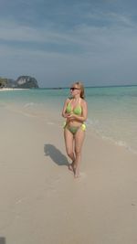 Full length of woman in bikini walking on shore at beach against sky