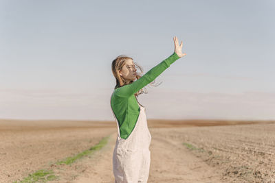 Young woman standing on dry field, shielding eyes