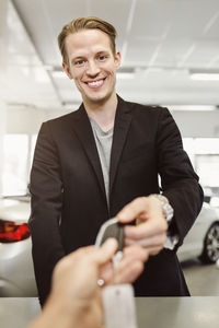 Portrait of happy man receiving keys from saleswoman in car dealership