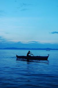 Silhouette man rowing boat in sea against sky during sunset