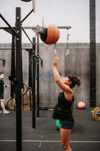 Side view of strong pregnant female athlete exercising with medicine ball in modern fitness center