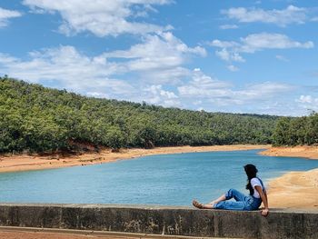 Man sitting on bridge over lake against sky