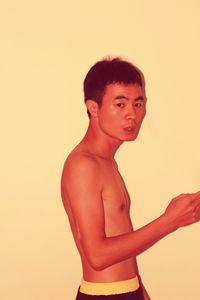 Portrait of shirtless man standing against yellow background