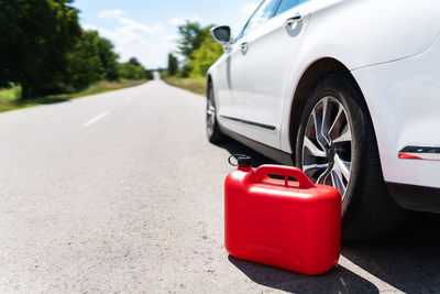 A car parked on the side of the road, an empty red canister. the driver is on the road. 