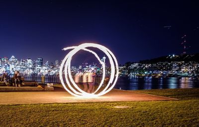 Light trails on illuminated city against clear sky at night