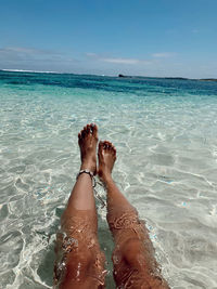 Low section of person relaxing in sea against sky