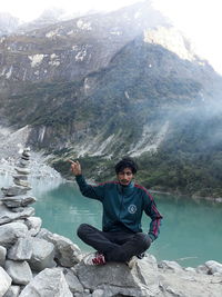 Young man sitting on rock against mountains