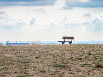 Empty wooden bench with view of sea and cargo ship on horizon