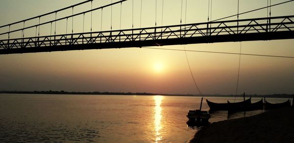 Silhouette bridge over sea against sky during sunset