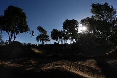 Low angle view of silhouette trees on landscape against clear blue sky