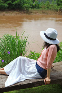 Woman in hat sitting against lake