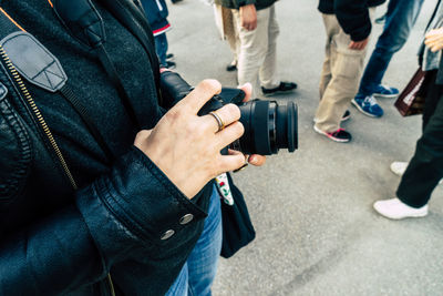 Midsection of woman holding digital camera while standing on street