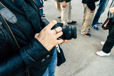 Midsection of woman holding digital camera while standing on street