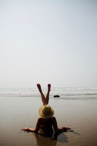 Rear view of young woman enjoying at beach against clear sky