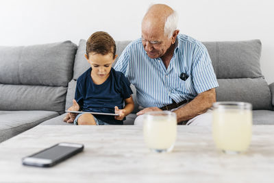 Grandfather and grandson sitting together on the couch at home looking at digital tablet