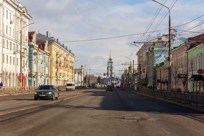 Cars on street by buildings in city against sky