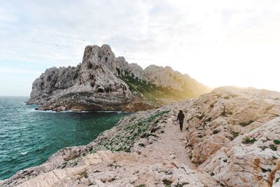 Woman walking on cliff at beach against sky