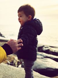 Cropped image of hand holding baby boy at beach