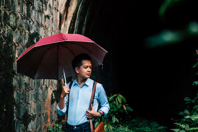 Young man looking away while standing in rain during rainy season