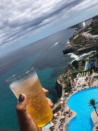 Close-up of hand holding drink at sea against sky