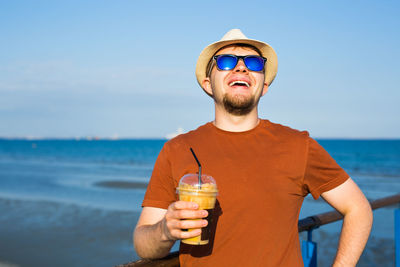 Young man wearing sunglasses against sky at beach