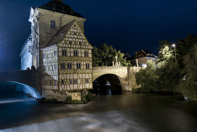 Illuminated building by river against sky at night