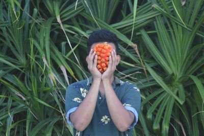 Man holding fruit in front of face against plants