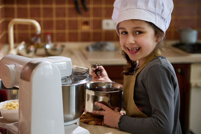 Portrait of young woman holding food in kitchen