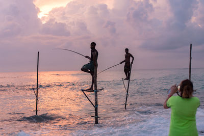 Men fishing on beach against sky during sunset