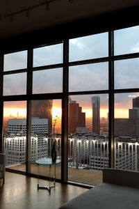 Buildings in city against sky during sunset seen through window