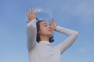 Portrait of young woman with arms raised against blue sky
