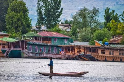 Man on boat by river against trees and buildings