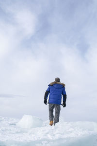 Rear view of man walking in snow against sky