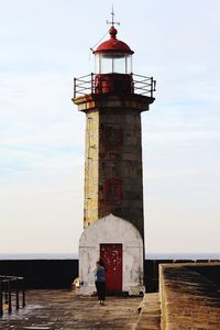 Man standing by lighthouse by sea against sky