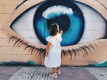 Rear view of woman standing against graffiti wall