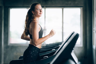 Portrait of smiling young woman running on treadmill