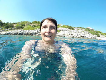 Portrait of senior woman swimming in sea against clear blue sky