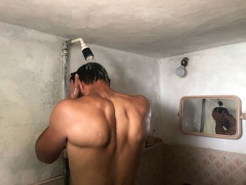 Rear view of shirtless man standing in bathroom