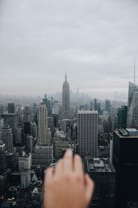 Close-up of hand over cityscape against cloudy sky